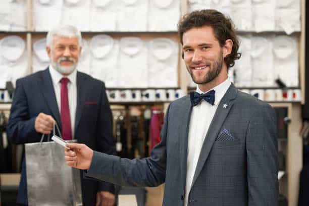 Homme en costume payant avec carte de crédit dans une boutique de vêtements pour hommes.